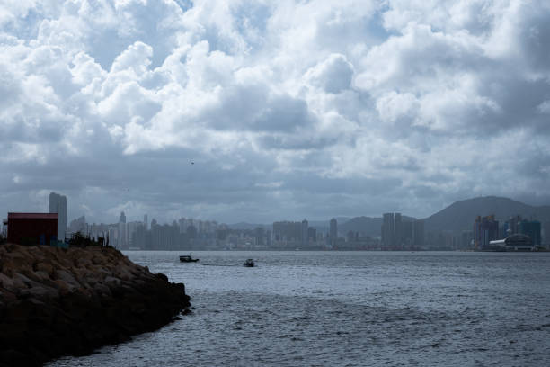 HONG KONG, CHINA. July 20, 2024. Hong Kong's eastern coast is beautifully captured in this image, where a sailboat sails through a tranquil harbor, framed by a lush hillside and a cityscape nestled along the shore.