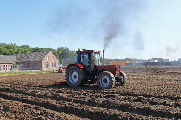 Potato harvesting in a field where one machine picks up the potatoes and loads them in a trailer pulled by a tractor that is waiting next to the field for the harvesting machine to bring the harvest.