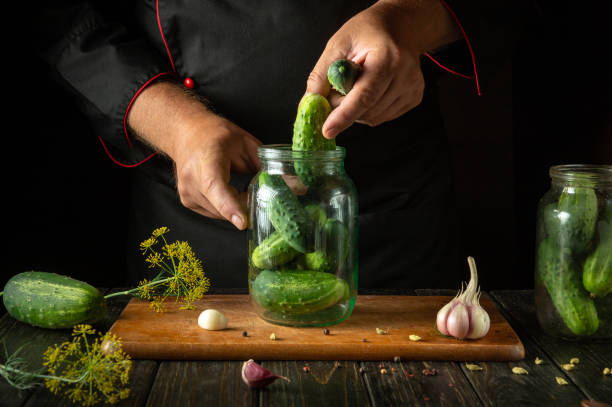 istock Preserving cucumbers in a jar by the chef's hands for long-term storage. The concept of pickling vegetables on the kitchen table 2166194582