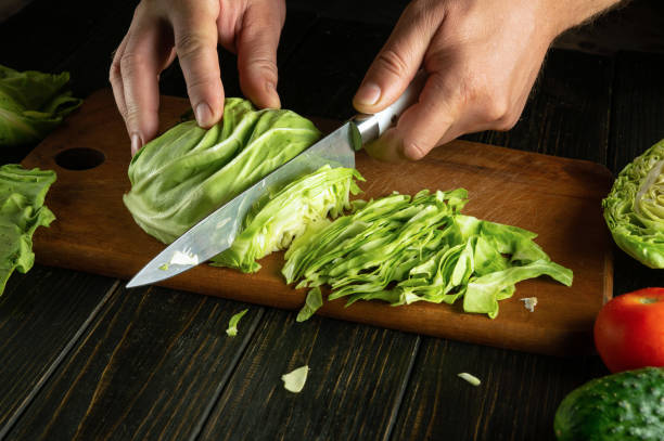 Chefs hands with a knife cut fresh cabbage on a kitchen board to prepare a vegetable salad for lunch at the hotel. Advertising space