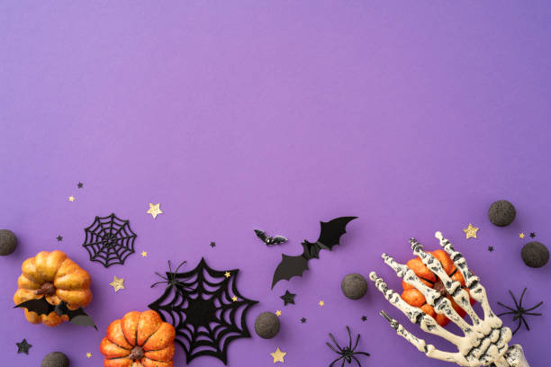 istock Halloween-themed background featuring pumpkins, bats, spider webs, skeleton hand, and holiday decorations on a purple surface 2166202839