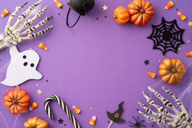 istock Festive Halloween background featuring pumpkins, skeleton hands, candy, and ghost cutouts on a purple backdrop 2166202846