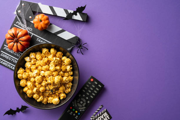 istock A bowl of popcorn, remote control, and Halloween decorations arranged on a purple background for a spooky movie night 2166202893