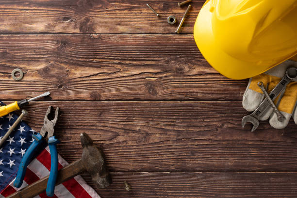 Labor Day themed image featuring various tools, a yellow industrial helmet, and an American flag on a wooden surface