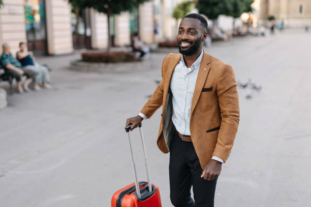 istock Man pulling red suitcase through city street view. 2166213956