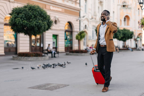 Man talking on phone pulling red suitcase, street walk.