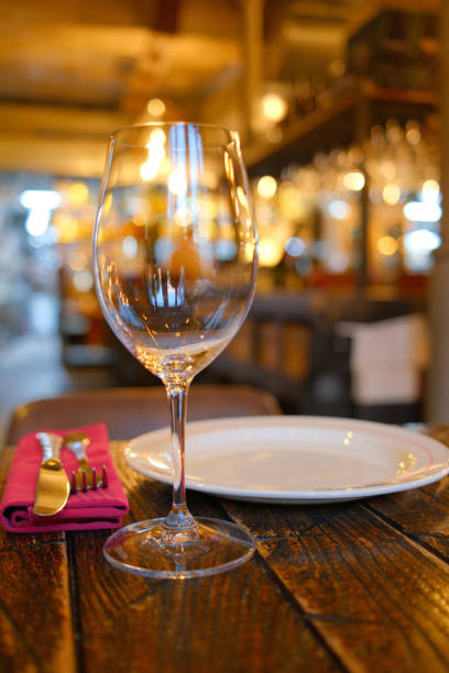 istock Elegant table setting in a cozy restaurant with empty wine glass, white plate, and silver cutlery on rustic wooden table 2166215921