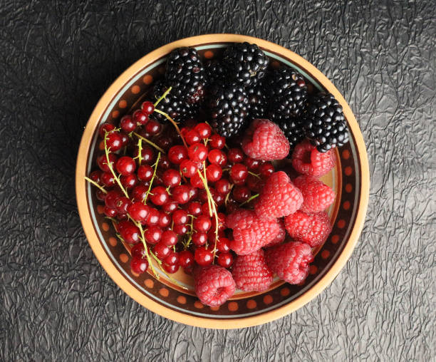 different berries in a wooden plate on a black background