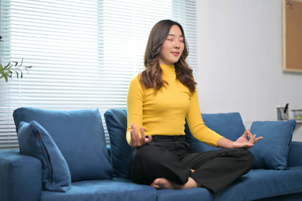 istock Woman Practicing Meditation on Blue Sofa in Bright Modern Living Room with Natural Light 2166227013