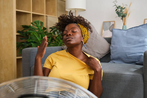 istock Young woman sweating suffering from heat wave at home using fan 2166229308
