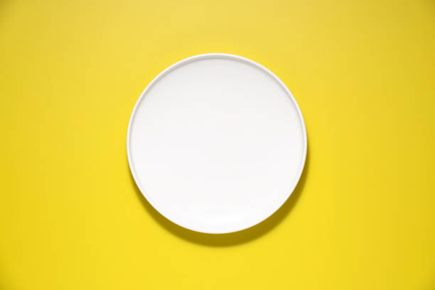 istock Top down view of a white plate isolated on yellow background with copy space 2166229679