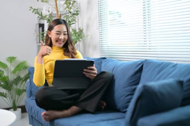 Young Woman Relaxing on a Blue Sofa Using a Tablet in a Bright Modern Living Room