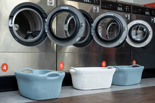 Empty washing machines built in row in self-service collective automatic laundry with baskets near them