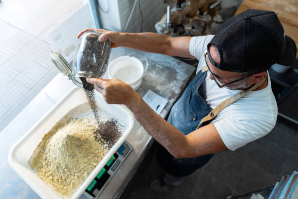 Top view of a baker adding ingredients to a dough while measuring the weight on an electronic scale.