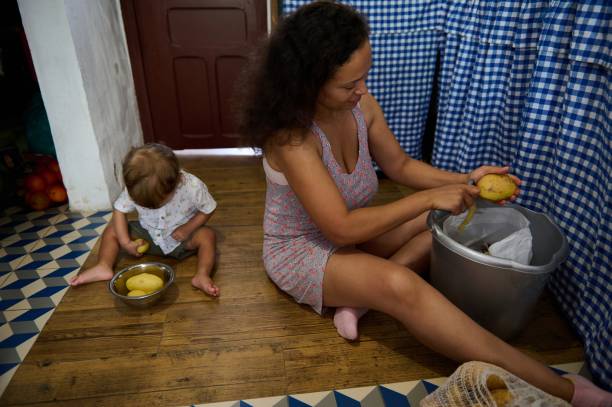 A mother and her child peel potatoes in a warm and homely kitchen. They share a moment of bonding as they prepare food together. The scene reflects family life and domestic chores.
