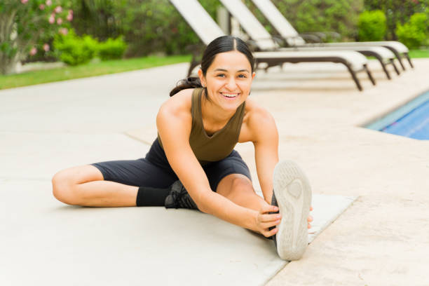 Athlete wearing black sleeveless tank top stretching legs after workout, warming up at sport stadium . Outdoors training. Morning routine. Healthy and sport lifestyle concept.