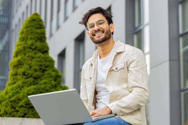 istock Indian man freelancer working on laptop computer sends messages reading email outdoors on bench 2166247404