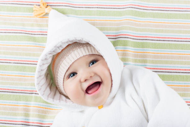 Adorable baby in white sunny bedroom. Newborn child relaxing in bed. Nursery for young children. Textile and bedding for kids. Family morning at home. New born kid during tummy time with toy bear.