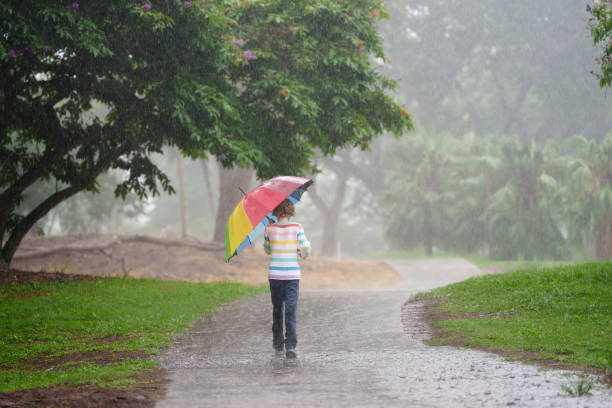 Child playing in autumn rain. Kid jumping in muddy puddle in beautiful park. Little boy with colorful umbrella under heavy fall shower. Stormy rainy weather fun.