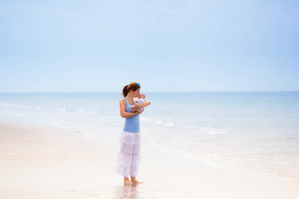 Mother and newborn child walking on beautiful beach. First vacation with baby. Travel with infant kid. Active fit mom after birth. Summer holiday family fun.