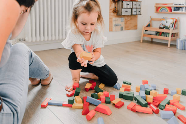 istock Little girl playing with building blocks while her mother is watching her 2166259166