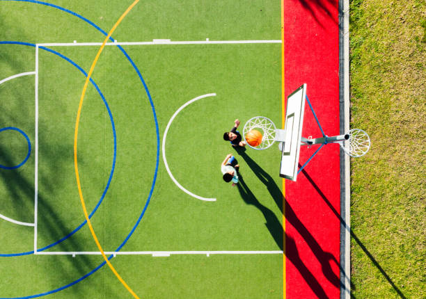 Top view of two boys playing basketball on a colorful outdoor court with distinctive circular and straight lines.