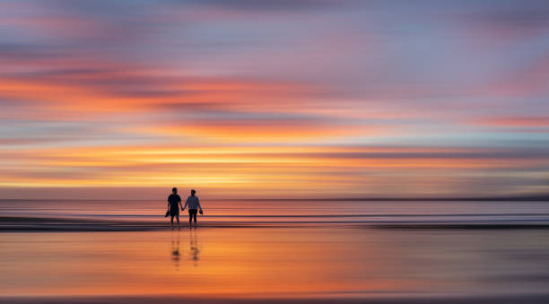 istock Couple holding hands, walking with reflection on a wet sandy beach. Blurred soft background. 2166284970