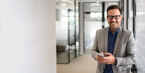 istock Successful male CEO messaging over cellphone and looking at camera while standing in office corridor 2166286866