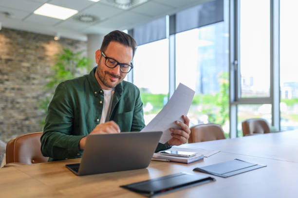 istock Handsome IT engineer in eyeglasses smiling and developing online website over laptop on desk in office 2166287015