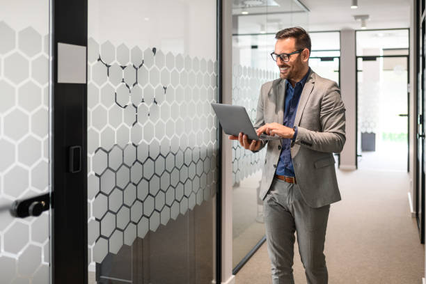 istock Smiling young businessman in eyeglasses working on his computer while walking in office corridor 2166287080