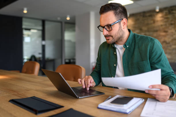 istock Financial advisor with glasses analyzing reports over laptop computer while sitting at desk in office 2166287186