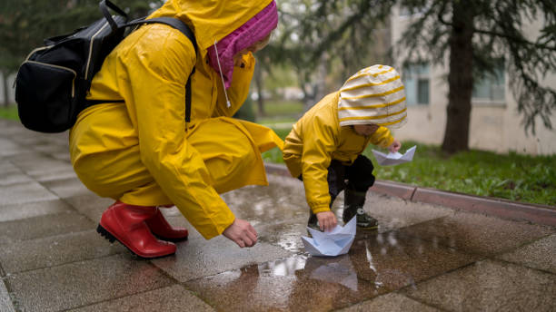 It's springtime. A small child in rubber boots jumps through puddles, plays and launches paper boats on the water.