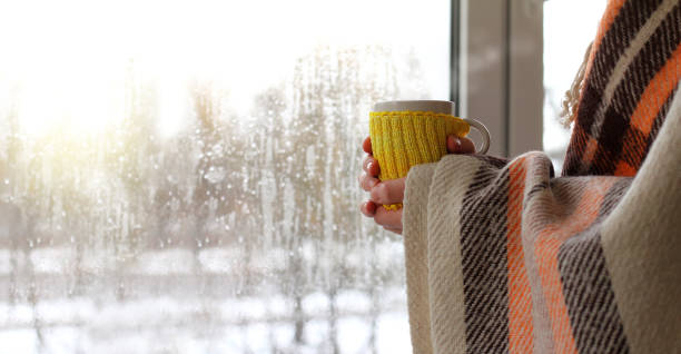 warming atmosphere with a hot drink unrecognizable man in a blanket with a mug in his hands against the background of a window with raindrops on a cold day cup of tea hands stock pictures, royalty-free photos & images