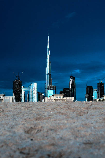 Burj Khalifa seen from the beach in Jumeriah 1. Taken from a low angle with the beach sand in the foreground. The Burj Khalifa dominates the skyline, with other tall skyscrapers also seen nearby. The daylight is fading, and the sky is a dark blue.