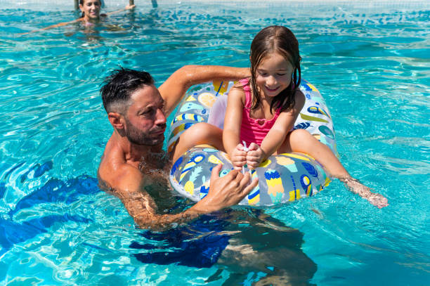 istock Father playing with daughter on inflatable ring in swimming pool 2166300225