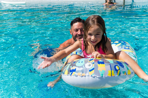 istock Dad pushing daughter on inflatable ring in swimming pool 2166300228