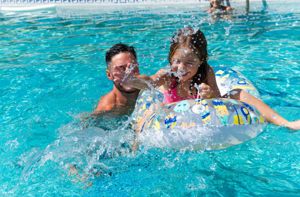 istock Dad splashing daughter playing with inflatable ring in swimming pool 2166300235