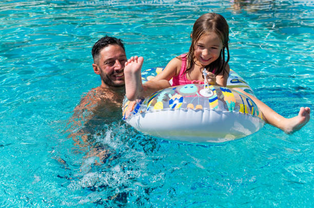istock Dad pushing daughter on inflatable ring in swimming pool 2166300240