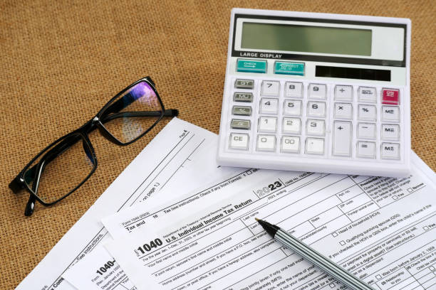 istock 1040 Tax Return document form on a burlap mat table with calculator and glasses 2166302118