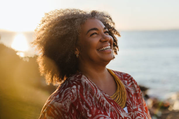 smiling mature woman enjoying healthy living by the sea at sunset - mulheres-maduras imagens e fotografias de stock