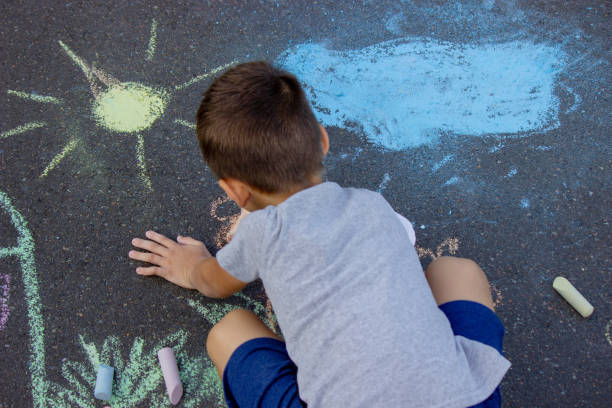 the boy draws with chalk on the asphalt. Selective focus.