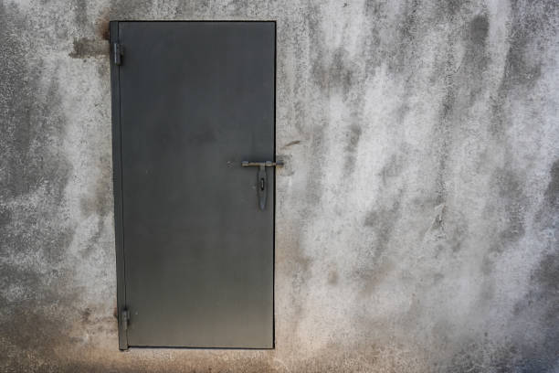 Locked gray metallic door installed on rough cement wall. Concept for security and privacy.