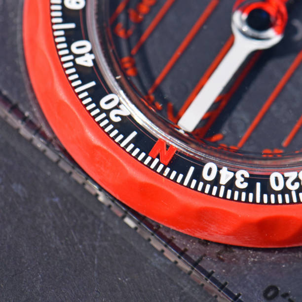 Part of a red manual or analogue compass with arrow pointing in the direction of north. Illustrates outdoor pursuits requiring navigation. Macro close up.
