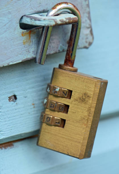 Open old brass numerical combination padlock on the latch for a green wooden shed door. Day outdoors. Close up.