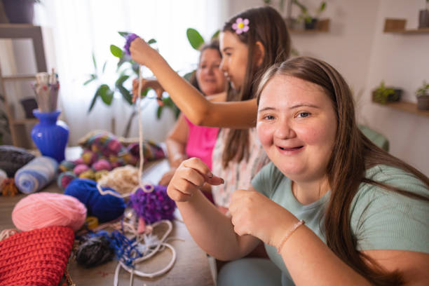 A loving mother patiently teaches her two daughters, including one with Down syndrome, how to knit, creating a moment of connection.