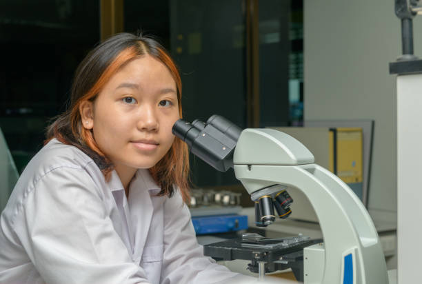 istock Cute scientist schoolgirl in lab coat looks through microscope for study microbiology in laboratory. 2166339106