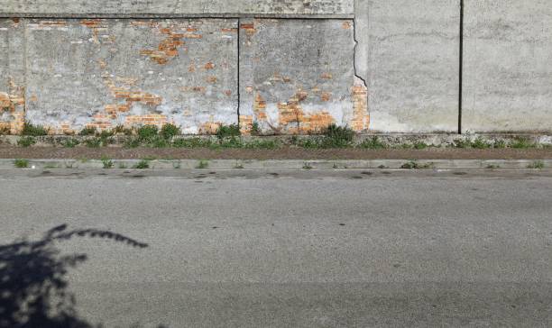 Weathered  wall with peeled plaster and some bricks exposed. Sidewalk and street in front. Grunge background for copy space.