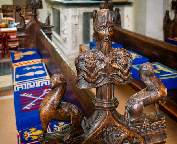 An old carved wooden pew end in the church of St Mary of the Assumption in Ufford, Suffolk, Eastern England. Colourful hassocks (kneelers) are on the pews.