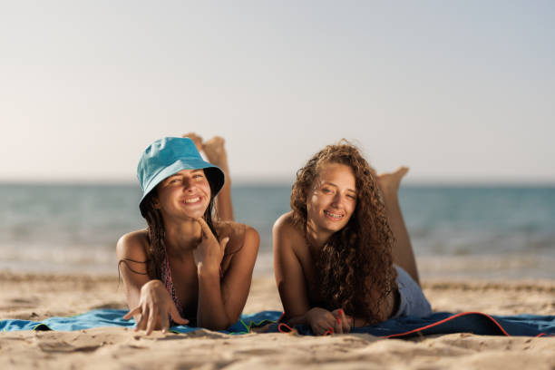 istock Two smiling young girls lying on a sandy beach on a sunny day 2166353184