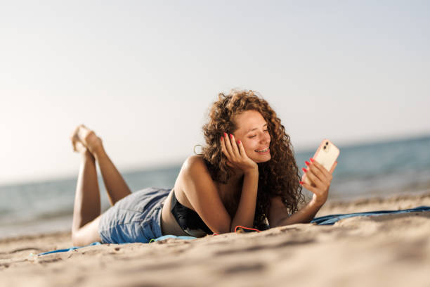 istock Smiling woman enjoying a summer day at the beach while using her smartphone 2166353232